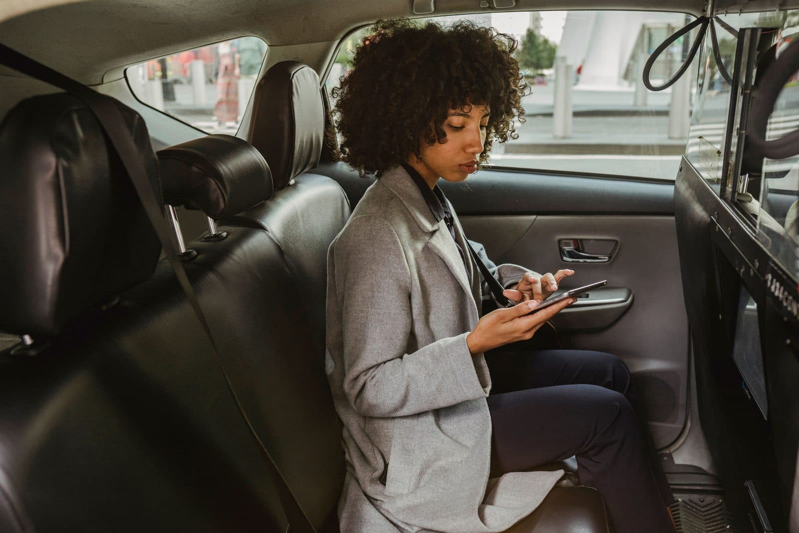 Passenger sitting in the back seat of a rideshare-style vehicle while using a phone